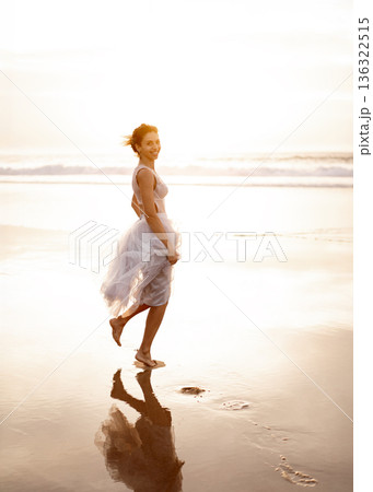 Smiling woman in white dress walking on wet sand 136322515