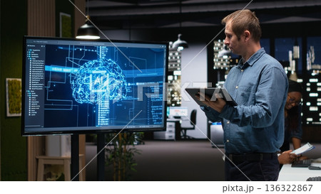 Manager in office using screen to analyze machine learning algorithms built by workers. Startup team leader supervising code written by employees to improve artificial intelligence 136322867