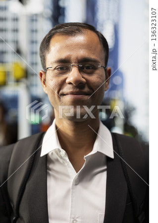 Portrait of indian businessman in suit standing on the sidewalk downtown, walking across metropolitan area business district. Male professional on a busy crowded street during commute. 136323107