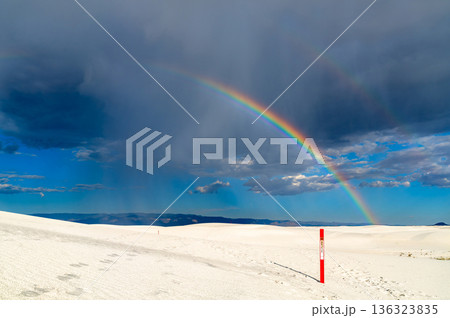 Alkali Flat Trail in White Sands National Park, New Mexico. Scenic view features a vivid rainbow over white gypsum dunes and a red trail marker under a stormy sky Alkali Flat Trail in White Sands National Park, New Mexico. Scenic view features a vivid rainbow over white gypsum dunes and a red trail marker under a stormy sky 136323835