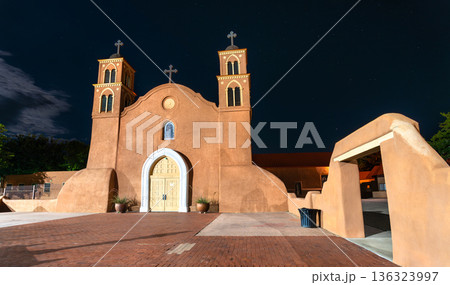 Old San Miguel Mission church in Socorro, New Mexico. Historic adobe architecture features twin towers and a white arch entrance under a starry night sky Old San Miguel Mission church in Socorro, New Mexico. Historic adobe architecture features twin towers and a white arch entrance under a starry night sky 136323997