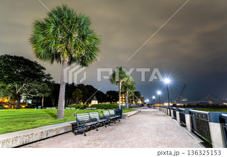Charleston Waterfront Park features a paved promenade with palm trees and benches leading to the Pineapple Fountain and Ravenel Bridge at night. South Carolina, USA Charleston Waterfront Park features a paved promenade with palm trees and benches leading to the Pineapple Fountain and Ravenel Bridge at night. South Carolina, USA 136325153