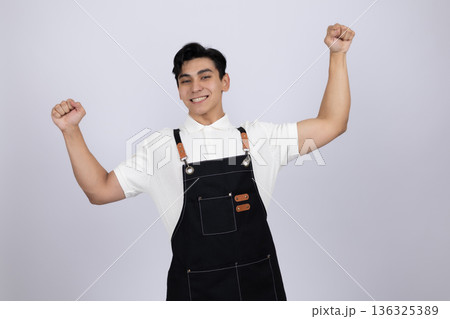 Excited young man in apron celebrating with arms up 136325389