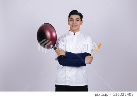 Chef holding a frying pan and wooden spoon playfully Chef holding a frying pan and wooden spoon playfully 136325405