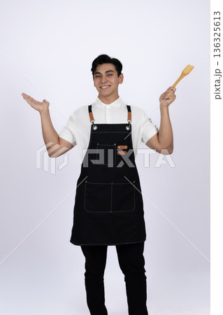 Happy young man in apron showing open palms gesture Happy young man in apron showing open palms gesture 136325613