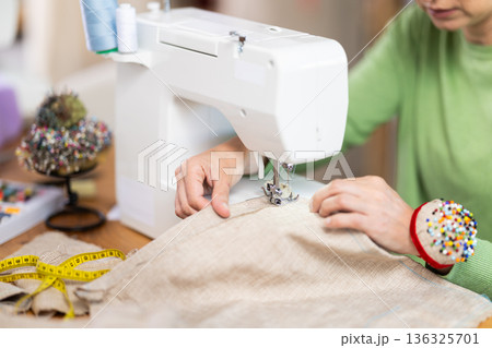 Closeup of woman hands and sewing machine - process of making clothes Closeup of woman hands and sewing machine - process of making clothes 136325701
