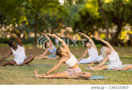 Girl stretching in Janu Sirsasana during group yoga in park Girl stretching in Janu Sirsasana during group yoga in park 136325803