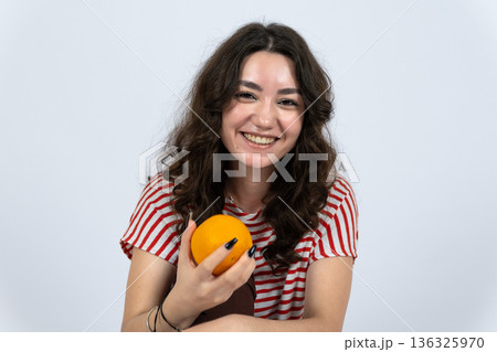 Smiling woman enjoying fresh orange fruit in studio Smiling woman enjoying fresh orange fruit in studio 136325970