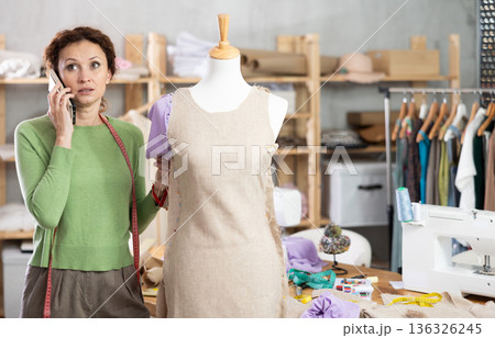 Woman seamstress talks on phone in workshop Woman seamstress talks on phone in workshop 136326245