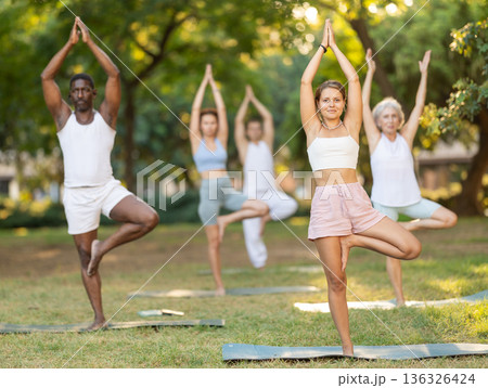 Girl doing Vrikshasana at group yoga session in park Girl doing Vrikshasana at group yoga session in park 136326424