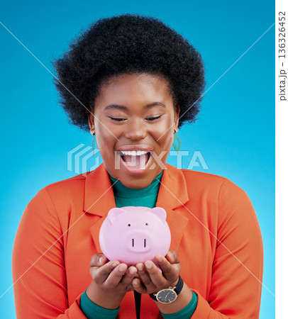 Woman, piggy bank and wow for savings, financial investment and profit, increase or budget success. Excited african person with banking goals, finance safe and container on a blue, studio background 136326452
