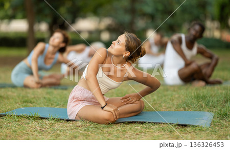 Multinational yoga enthusiasts with female coach perform padmasana in park Multinational yoga enthusiasts with female coach perform padmasana in park 136326453
