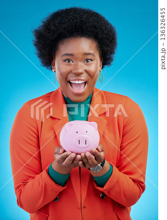 Woman, piggy bank and wow portrait for savings, financial investment and profit or budget success. Excited african person with banking goals, finance safe and container on a blue, studio background Woman, piggy bank and wow portrait for savings, financial investment and profit or budget success. Excited african person with banking goals, finance safe and container on a blue, studio background 136326455