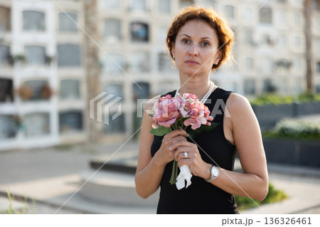 Woman in black mourning dress standing with flowers near columbarium Woman in black mourning dress standing with flowers near columbarium 136326461