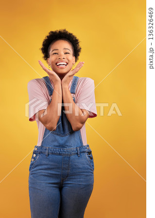 Wow, celebration and hands on face of black woman in studio happy for news, deal or promo on yellow background. Portrait, smile and African female winner excited for lottery, coming soon or bonus 136326469