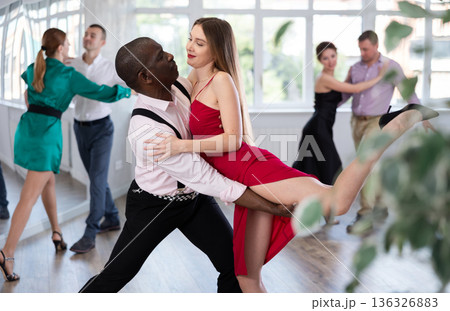 Elegant duet of man and woman in festive dresses dances passionate tango during group dance lesson in choreographic studio 136326883