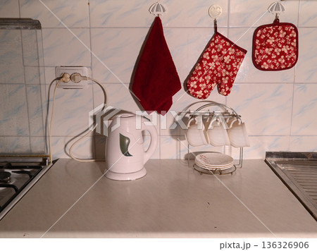 a white electric kettle and a stand with cups on a kitchen countertop near the wall 136326906