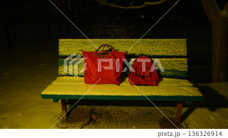 red bags on a snowy bench at night 136326914