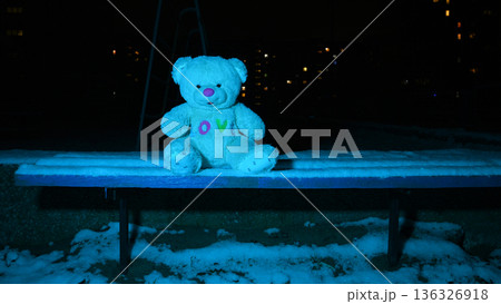 teddy bear sitting on a long bench on a winter night 136326918