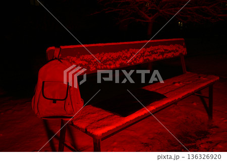 backpack hanging on the back of a snowy bench in red light 136326920