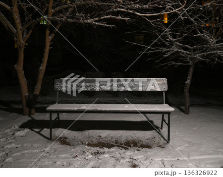 empty wooden bench covered with frost and snow in the night park 136326922