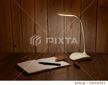 white desk lamp illuminates an open notebook on the table 136326923