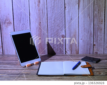 white tablet on a stand next to an open notebook and a blue pen 136326928