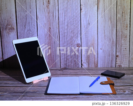 tablet in a white frame on a stand with a notebook on a wooden surface tablet in a white frame on a stand with a notebook on a wooden surface 136326929