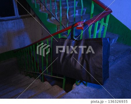 large black bag hanging on the stairs railing in blue light large black bag hanging on the stairs railing in blue light 136326935