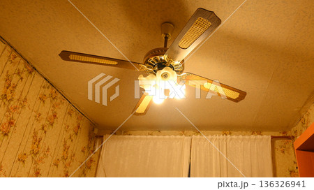 a ceiling fan with four blades and lamps turned on under a yellow ceiling 136326941