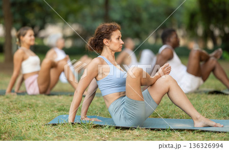 Multinational yoga enthusiasts with female coach perform hindolasana in park 136326994