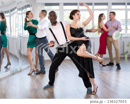 Elegant african american man performing kizomba paired with attractive woman in red in studio class setting Elegant african american man performing kizomba paired with attractive woman in red in studio class setting 136327055