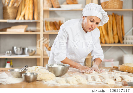 Female employee cooks croissants, rolls dough into tube, forms muffin from raw dough material 136327117