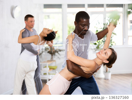 Positive African american man dancing playful Latin dance bachata with female partner during group class in choreography studio Positive African american man dancing playful Latin dance bachata with female partner during group class in choreography studio 136327160