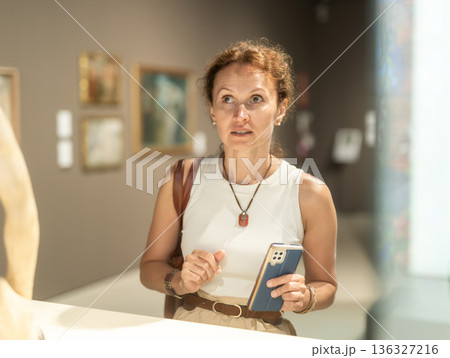 Woman with phone looking at museum exhibit 136327216