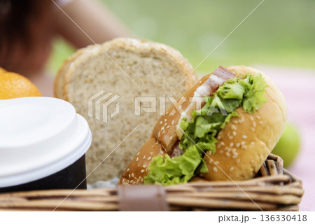 Picnic basket food bread fresh fruit coffee cup orange juice in wood wicker box on red Blanket. Wheat bakery fruit food and drinks in green park outdoor lifestyle. Breakfast healthy appetizer box. 136330418