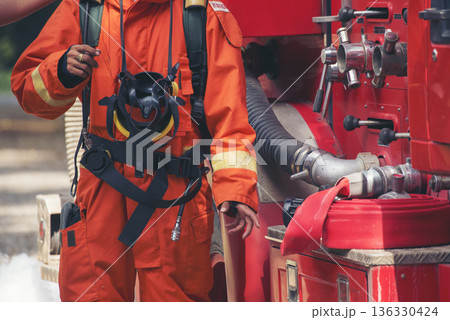 Fireman prepare equipment fighting extinguisher at fire engine truck. Firefighter fighting with smoke flame using fire hose, tube, chemical water foam spray at truck. Fireman wear hard hat protection 136330424