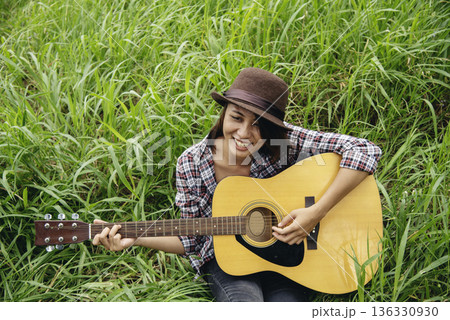 Young women playing acoustic guitar outdoor in green park. Woman person playing acoustic guitar music instrument at home, young Asian musician girl lifestyle in beautiful nature. Happy guitarist Young women playing acoustic guitar outdoor in green park. Woman person playing acoustic guitar music instrument at home, young Asian musician girl lifestyle in beautiful nature. Happy guitarist 136330930