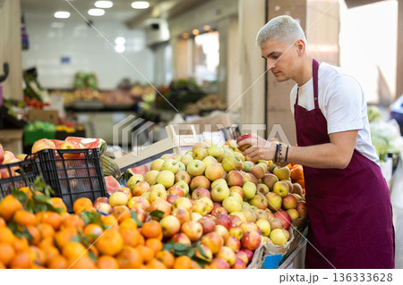 Young guy seller puts apples in vegetable shop 136333628