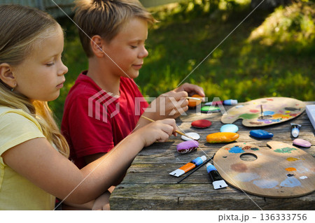 Focused Little Girl Painting Stone with Bright Acrylic Colors During Creative Art Activity at Easter DIY Craft Project for Kids, Childhood Learning and Fun Hobby Concept 136333756