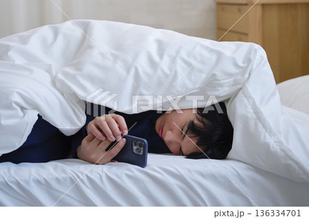 布団に包まってスマホを使う20代男性 布団に包まってスマホを使う20代男性 136334701