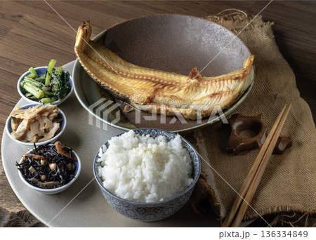 Presented alongside white rice, several small side dishes, and chopsticks, a large, golden-brown charcoal-grilled Atka mackerel (Shima Hokke). Presented alongside white rice, several small side dishes, and chopsticks, a large, golden-brown charcoal-grilled Atka mackerel (Shima Hokke). 136334849