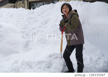 大雪の中でスコップを持って途方に暮れる女性 136335087