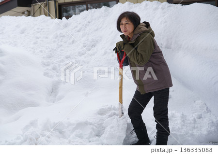大雪の中でスコップを持って途方に暮れる女性 136335088