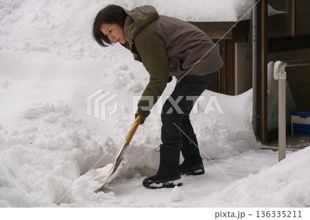 大雪の中でスコップで雪かきをする女性 136335211
