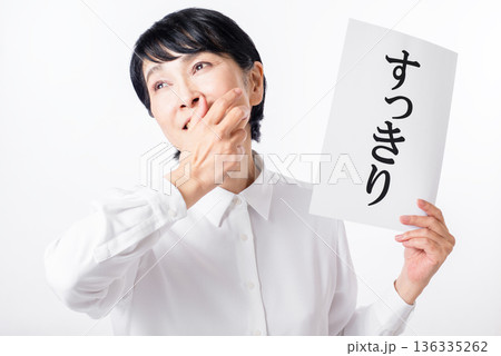 すっきりと書かれた紙を持ち口に手を添え笑う白いシャツを着たシニア女性 すっきりと書かれた紙を持ち口に手を添え笑う白いシャツを着たシニア女性 136335262