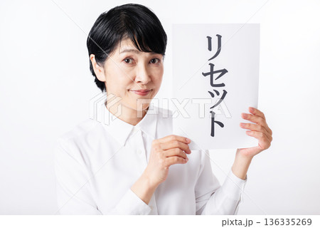 リセットと書かれた紙を両手で持ちカメラ目線のシニア女性 136335269