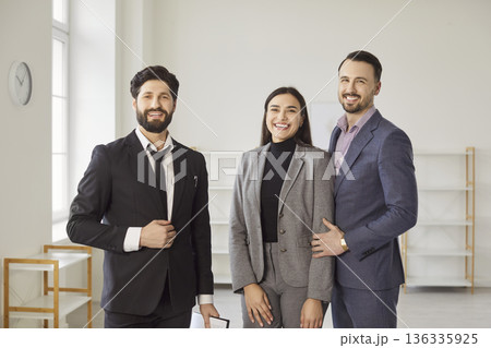 Young man realtor standing with happy couple looking at camera in new house. 136335925