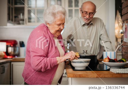 Elderly couple making dinner together in kitchen. Elderly couple making dinner together in kitchen. 136336744