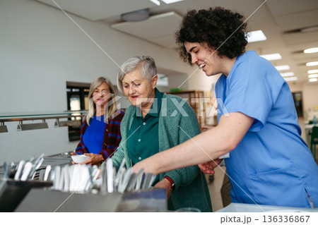 Caregiver helping older woman in community center cafeteria. Caregiver helping older woman in community center cafeteria. 136336867
